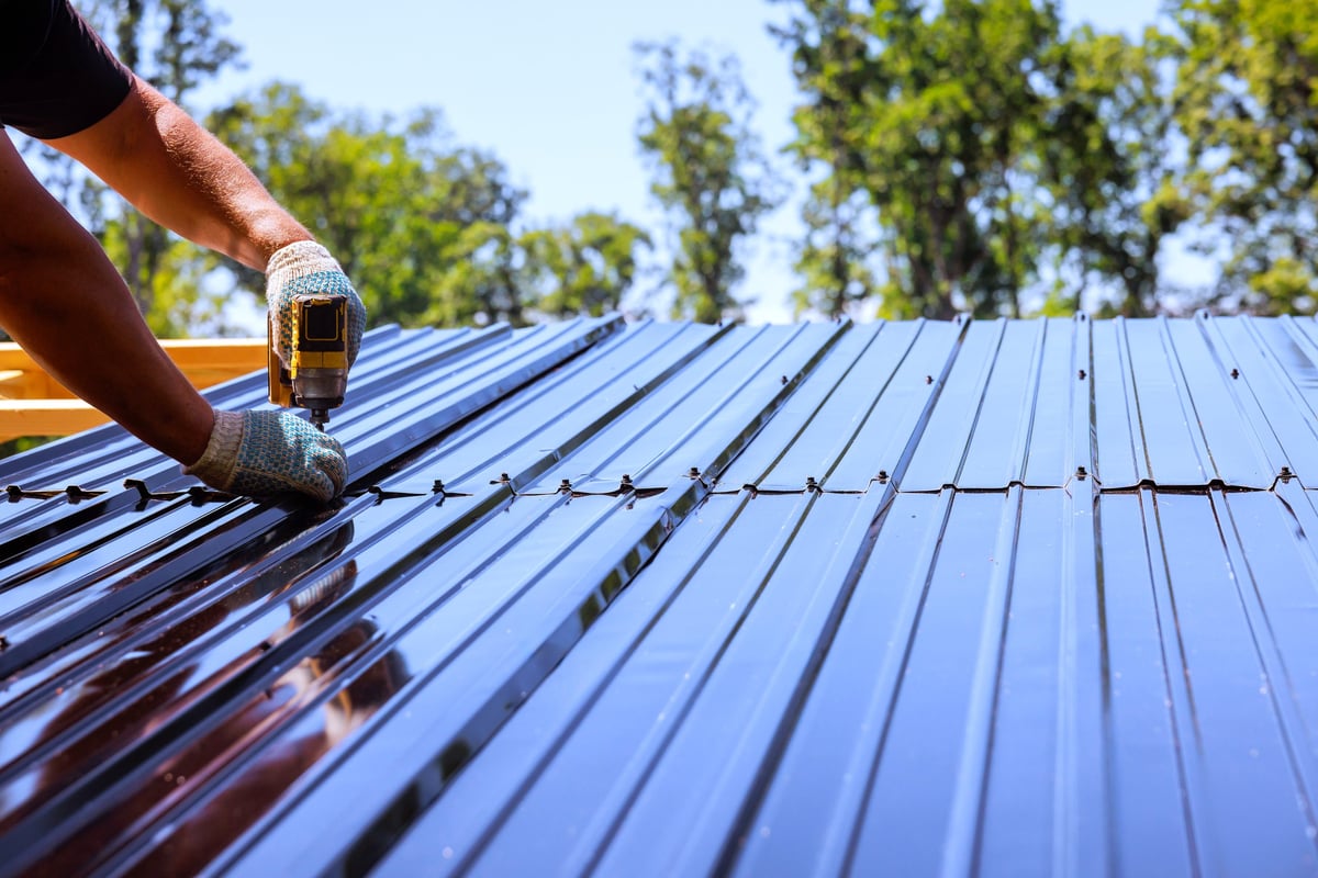 Contractor securing metal roofing sheets to house with power drill